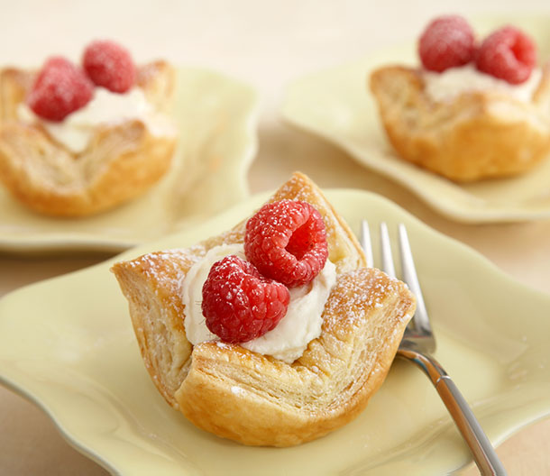An image of prepared Mini Puff Tartlets made with Pepperidge Farm® Puff Pastry Sheets, egg, cream cheese, confectioners' sugar, whipped topping and raspberries or semi-sweet chocolate.