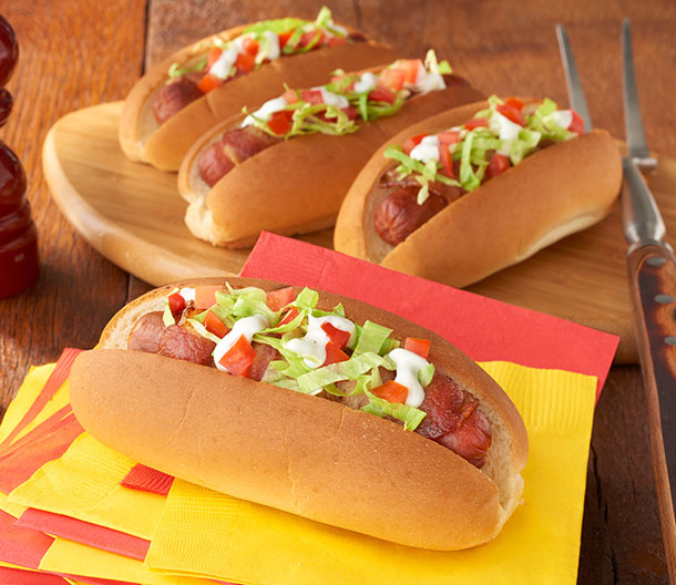 An image of prepared Ranch BLT Dogs made with bacon, hot dogs, Pepperidge Farm® Hot Dog Rolls, shredded lettuce, tomatoes and ranch dressing.